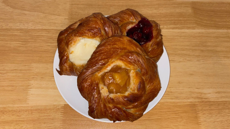 Three large danishes of different flavors on a white plate.