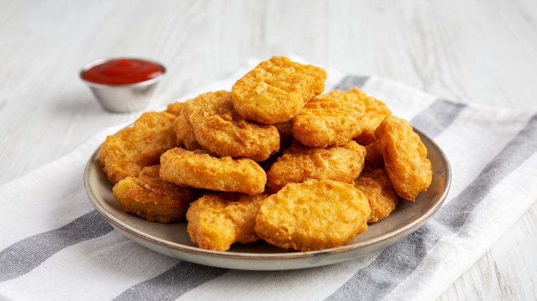 Chicken niggets piled on a plate with sauce in the background