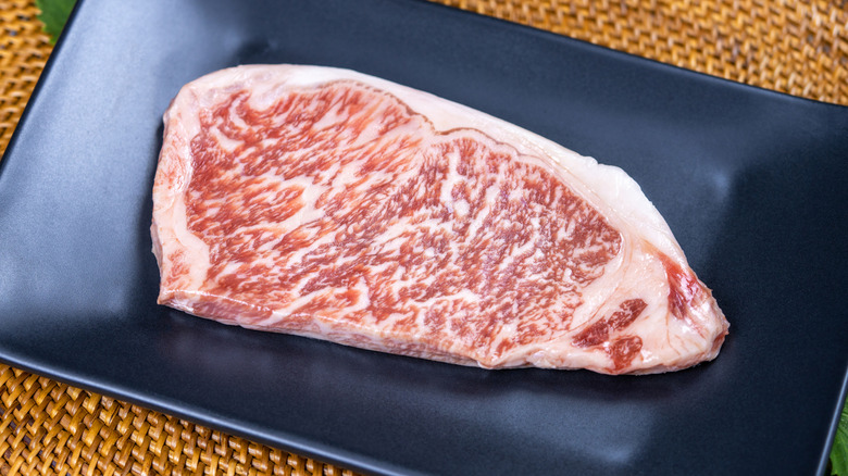 Raw wagyu strip steak on dark square plate