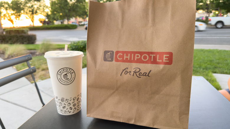 Chipotle-branded bag and cup on outdoor table.