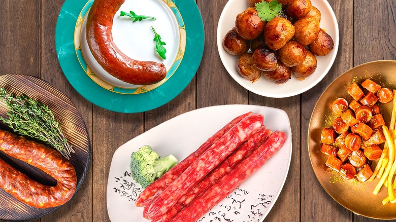 Several different plates of sausage sit on a table with green garnishes