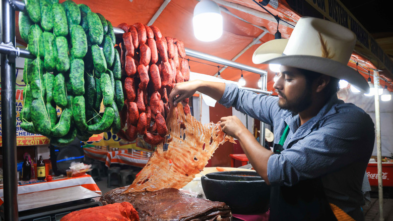 A man works a taco stand that has green and red chorizo