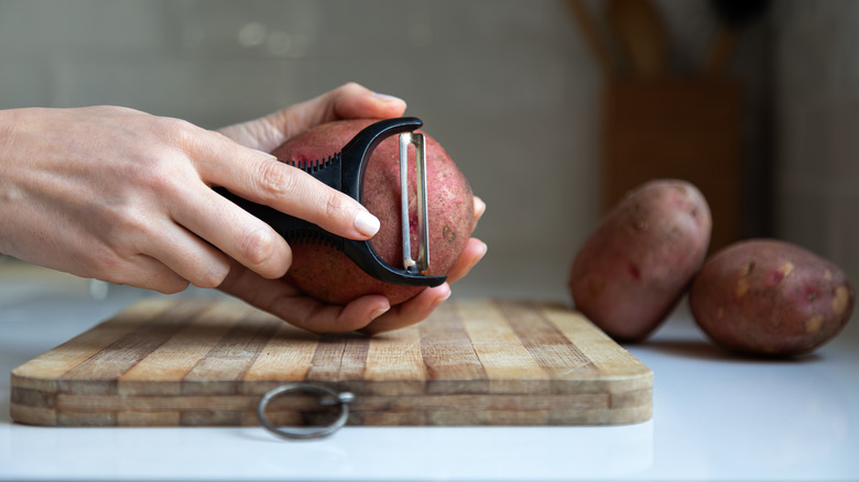 An illustrative image showing an individual peeling potatoes over a wooden board