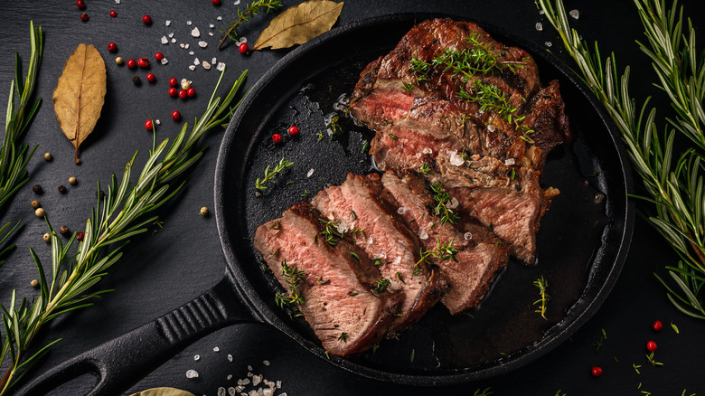 Steak slices in a pan are topped with herbs and photographed from above.