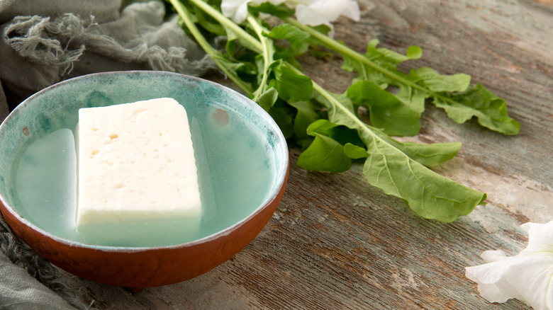 Feta cheese in a bowl of brine on a wooden table.