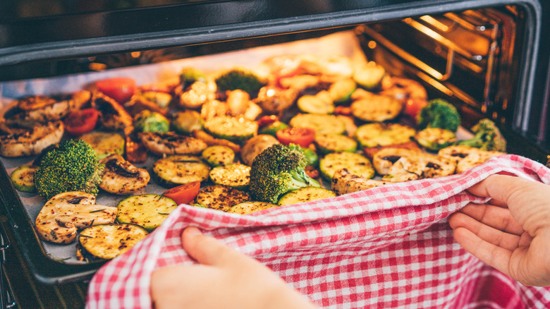 Hands removing a tray of roasted vegetables from the oven