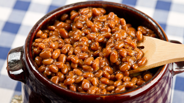 A pot of baked beans sits on gingham tablecloth