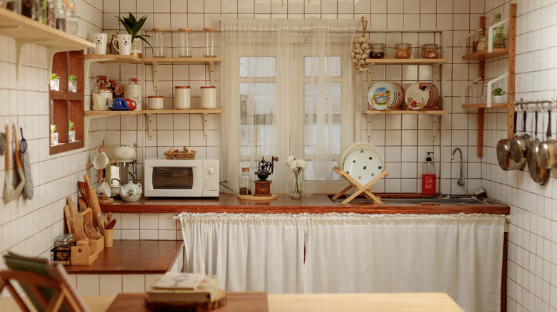 Small kitchen with open shelving and fabric accents, including sheer window curtains and cabinet curtains