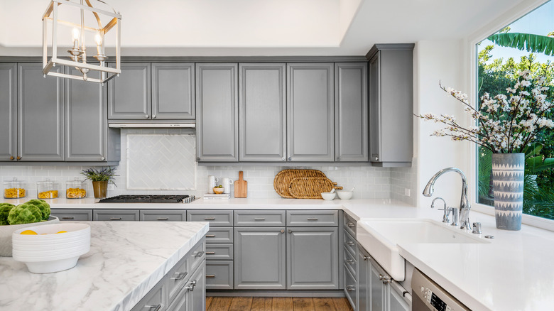 A gray and white kitchen with interesting additions of a cool light fixture, flowers, and other accessories that make the whole space more interesting