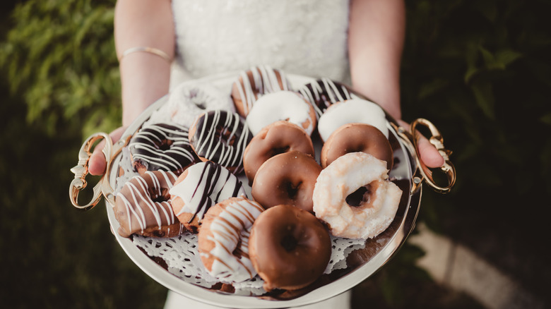 A bride holding out a plate of expertly crafted doughnuts
