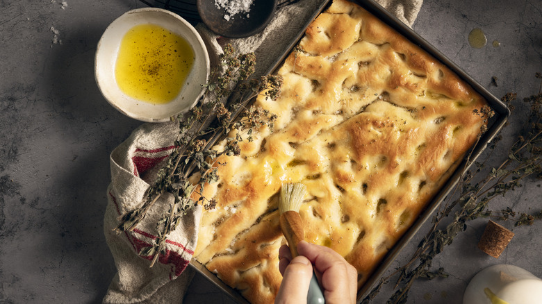 Freshly baked Italian flatbread being brushed with olive oil