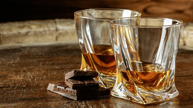 Two glasses of Scotch with some pieces of dark chocolate on a table