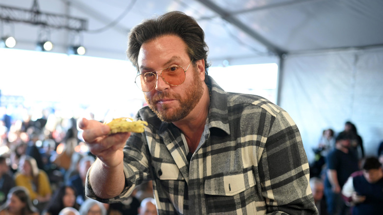 Scott Conant wearing sunglasses and holding a piece of food up to the camera