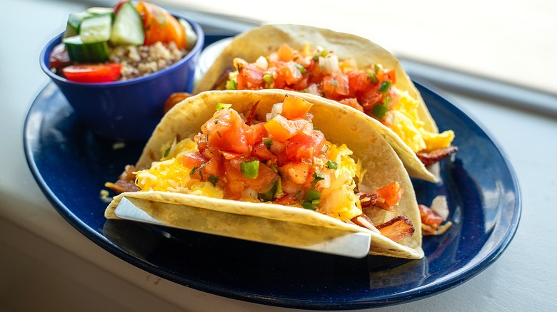 Two tacos with bacon, scrambled eggs, shredded cheese, and salsa on a dark blue plate