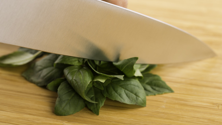 chef chopping basil on wooden chopping block