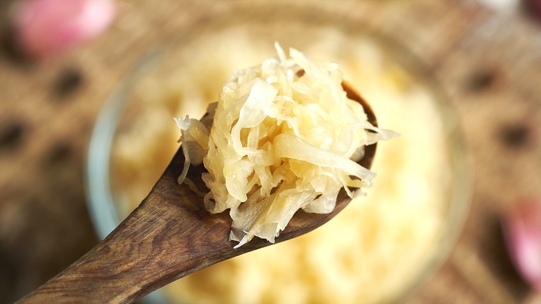 Close-up of a small wooden spoon with sauerkraut over a bowl of sauerkraut in the background