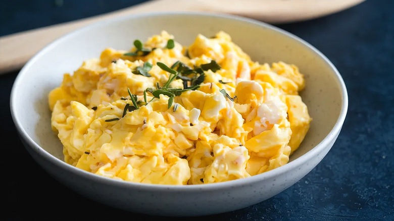 Scrambled eggs topped with fresh herbs in a bowl on a dark blue surface.