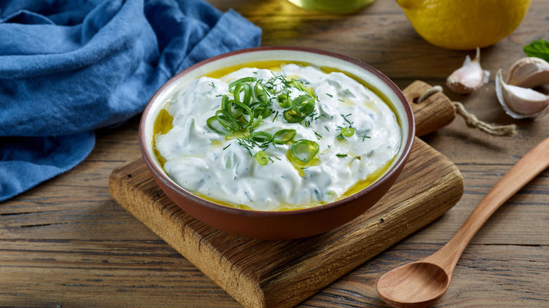 A bowl of tzatziki on a wooden cutting board.