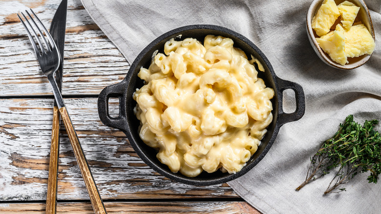 White cheddar macaroni and cheese in a cast iron pan with a fork and knife on the side