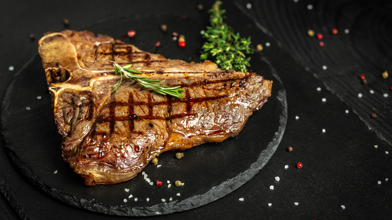 Cooked T-bone steak with herbs on a black stone cutting board