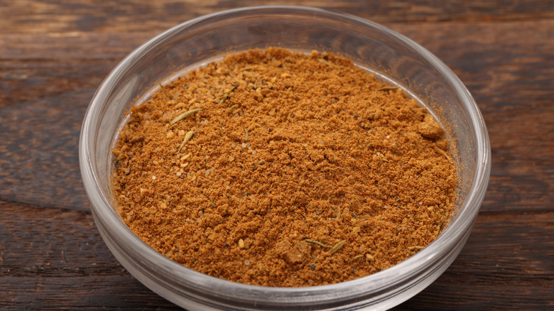 Cajun seasoning in a glass bowl on wood surface.