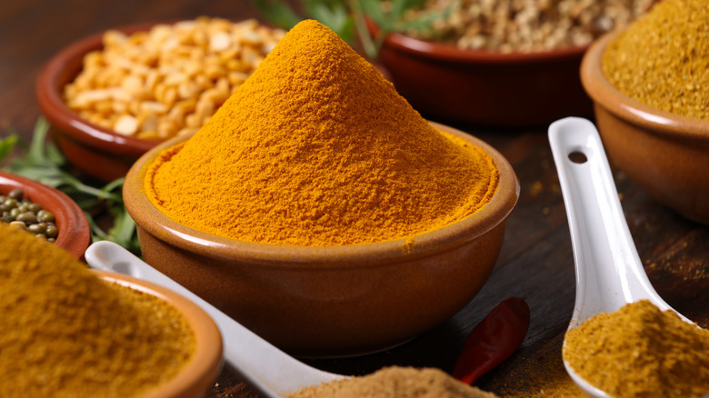 Pile of curry seasoning in a small ceramic container with white spoons.