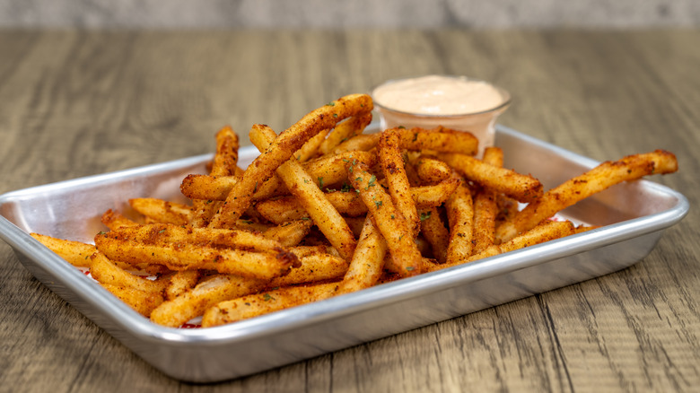 Seasoned fries and a jar of creamy sauce on tin tray.