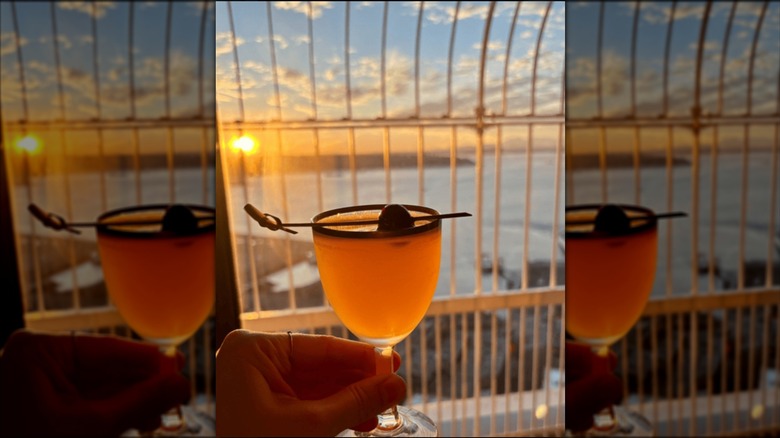 A cocktail held in front of a window at the Smith Tower Observatory Bar in Seattle at sunset.