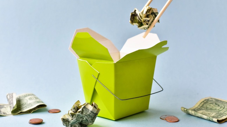 Chopsticks lifting dollar bills out of takeout box
