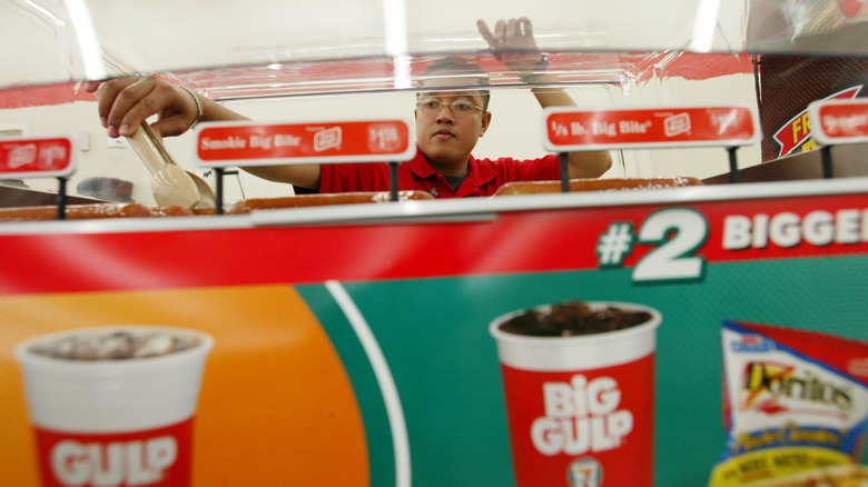 A worker selects a smokie from the 7-Eleven grill