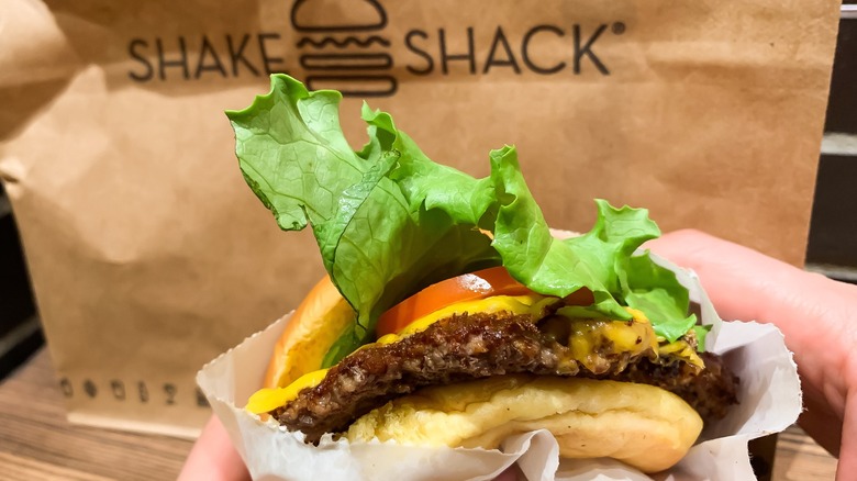 Hands hold a fresh burger in front of a paper Shake Shack bag