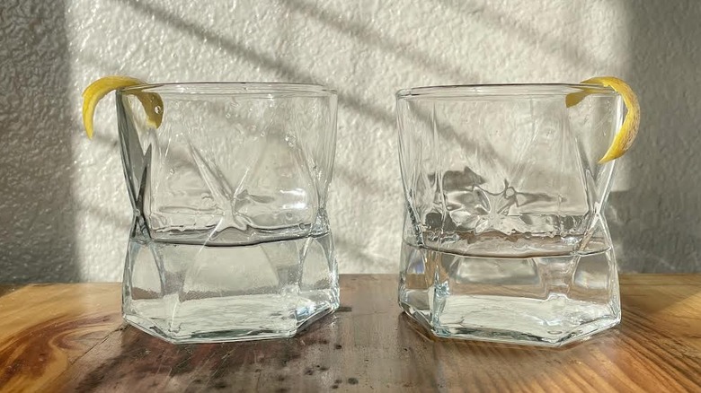 Two classic martinis with lemon swath garnishes on a wooden table.