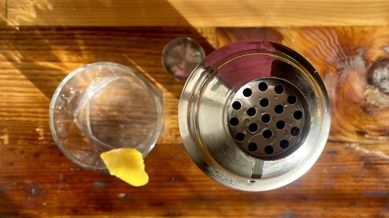 Overhead view of a classic martini with a lemon swath and a cocktail shaker.