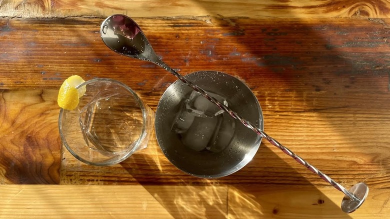 Overhead view of a classic martini with a lemon swath and a cocktail shaker with a spoon.