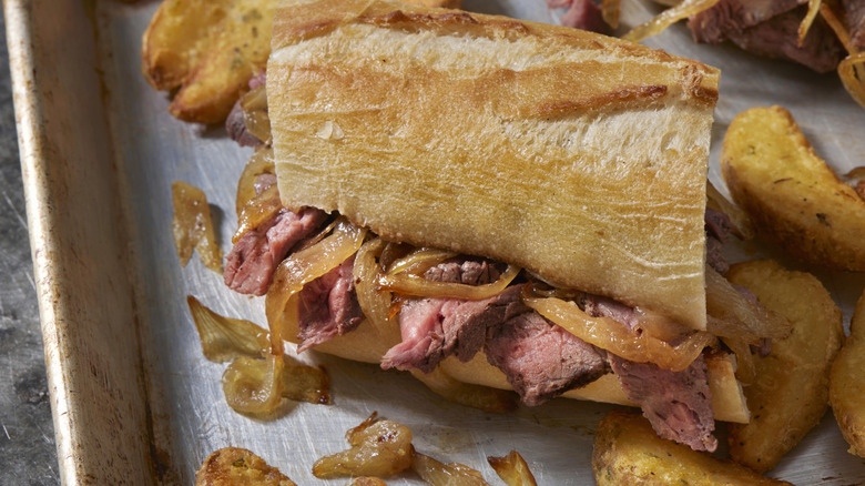 Steak sandwich and oven-baked fries on a sheet pan.