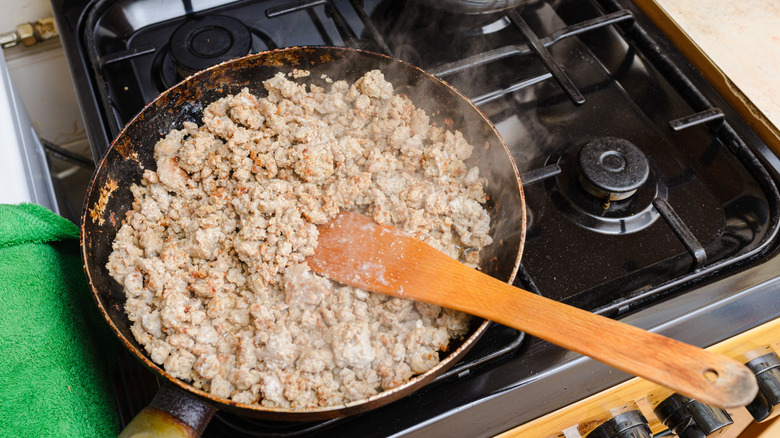 Ground beef sauteing on a stovetop with a wooden spatula.