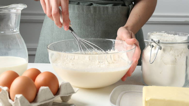 person mixing up cake batter with eggs, milk, and butter