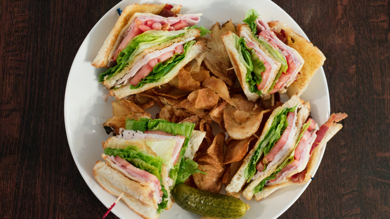 Club sandwich sliced into quarters with chips and a pickle