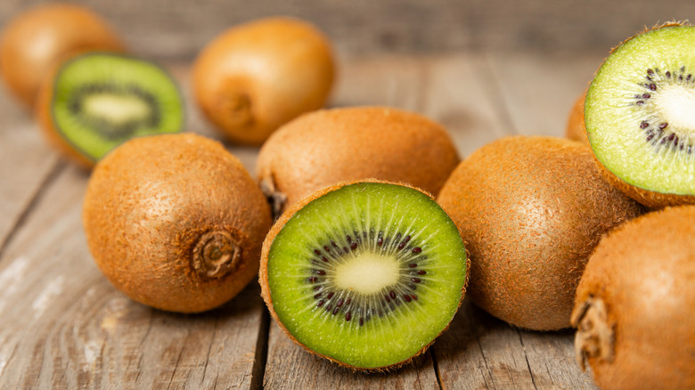 kiwis on a wooden surface, some sliced in half