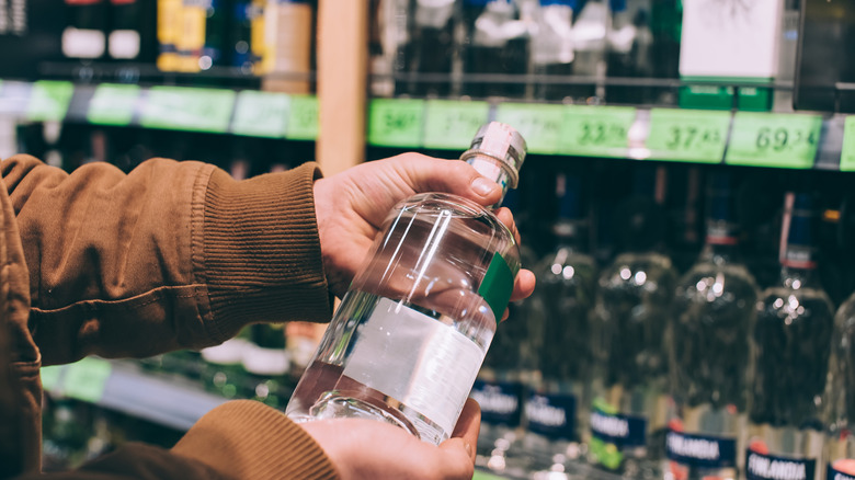 A person holding a bottle of vodka in front of a store's alcohol aisle