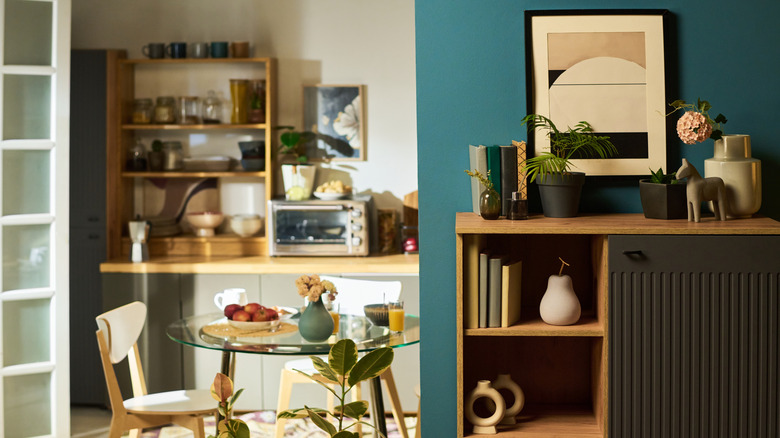 A cozy kitchen in the background with a partially visible artwork on the wall, and in the foreground, a sophisticated shelf