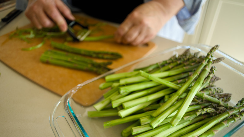 Person peeling asparagus spears on a cutting board.