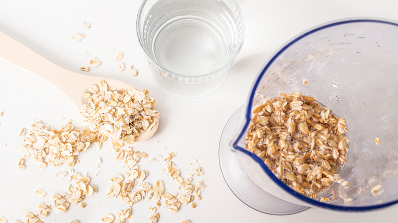 Dry oats on a spoon, a glass of water, and soaked oats in a measuring cup
