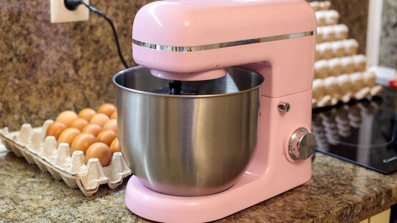 A pink stand mixer on a counter next to a package of eggs.