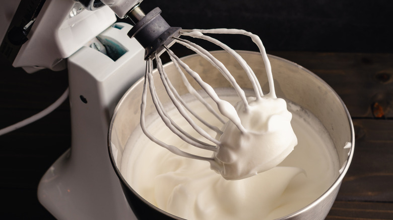 A stand mixer with a whisk coated in egg whites from its mixing