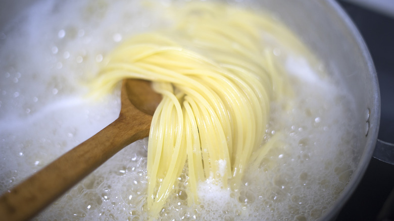 Wooden spoon scooping spaghetti noodles out of boiling water