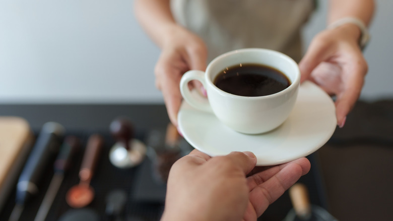 Close up of hands holding a white mug of black coffee on white saucer