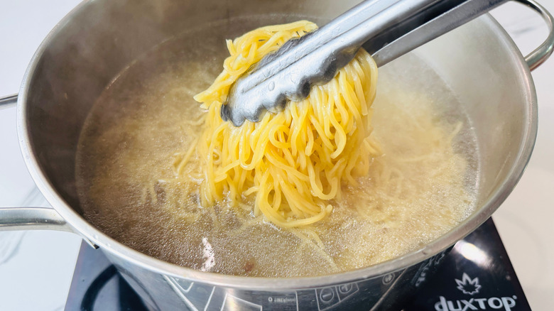 Tongs pulling noodles from pot of water