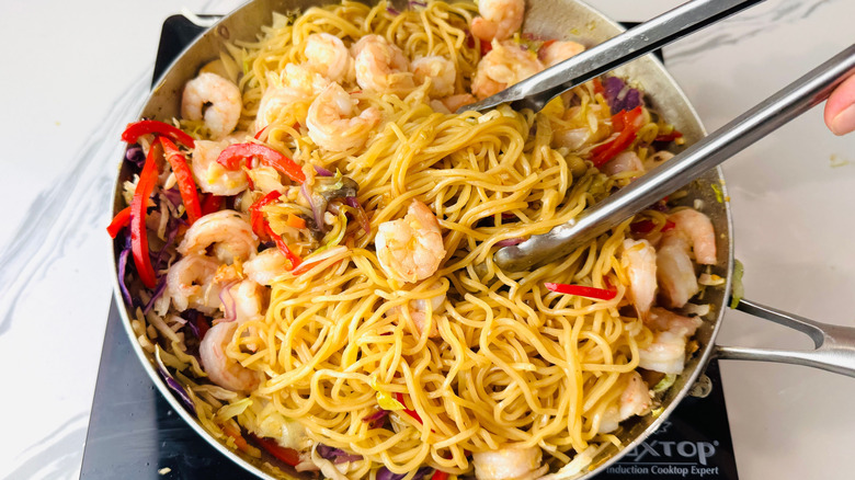 Tongs tossing shrimp lo mein in pan