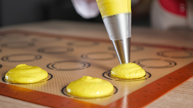 cookies being piped onto a silicone baking mat.
